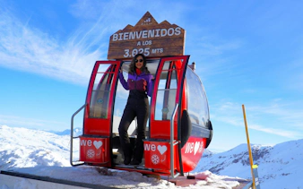 Tourist standing in a red gondola at Valle Nevado, Chile, with snowy mountains in the background.
