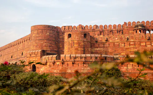 Agra Fort's red sandstone walls surrounded by greenery, part of the Same Day Taj Mahal tour from Delhi.