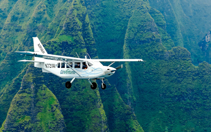 Small plane flying over lush green mountains in Kauai during air tour.