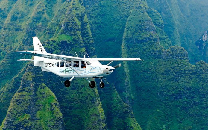 Small plane flying over lush green mountains in Kauai during air tour.
