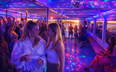 Lisbon boat party with DJ, colorful lights, and guests enjoying the sunset cruise.