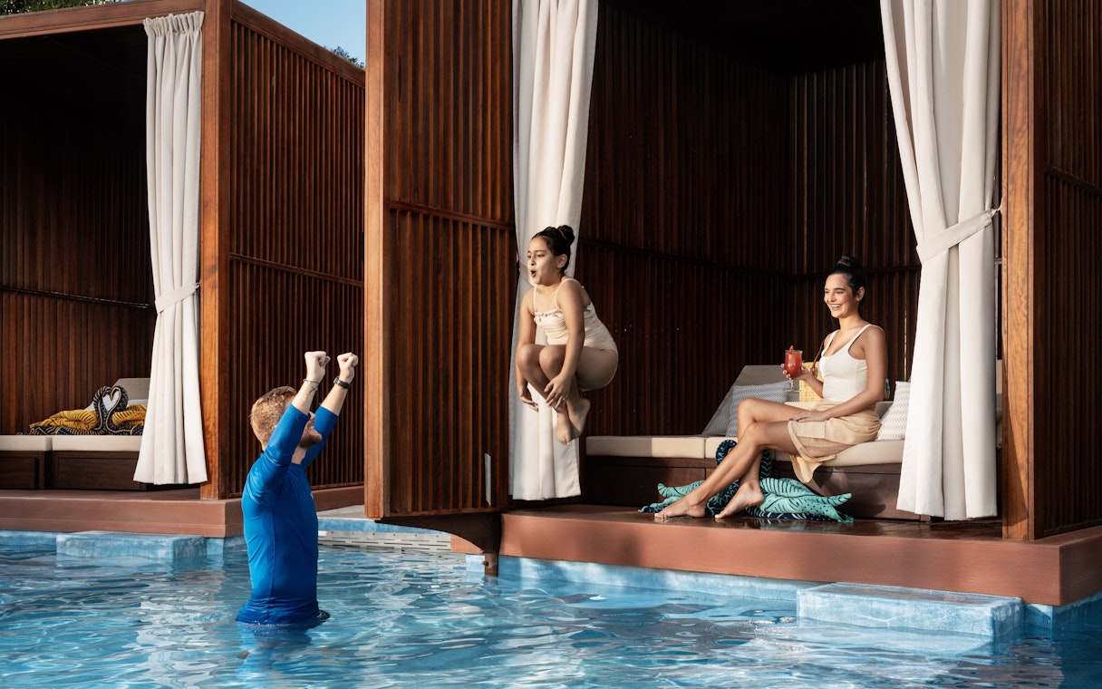 Girl jumping into pool as dad cheers at Grand Hyatt waterpark, Dubai.
