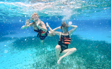 Two people snorkeling underwater with life vests in clear blue ocean.