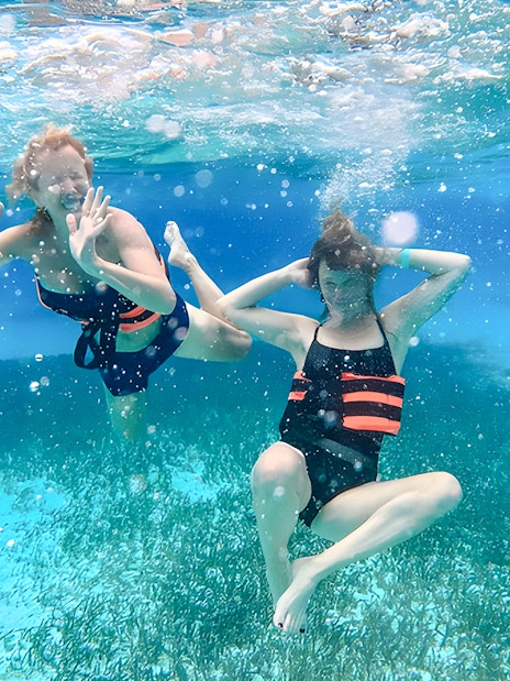 Two people snorkeling underwater with life vests in clear blue ocean.