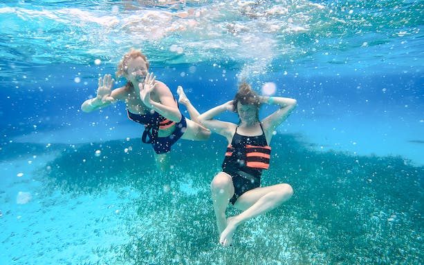Two people snorkeling underwater with life vests in clear blue ocean.