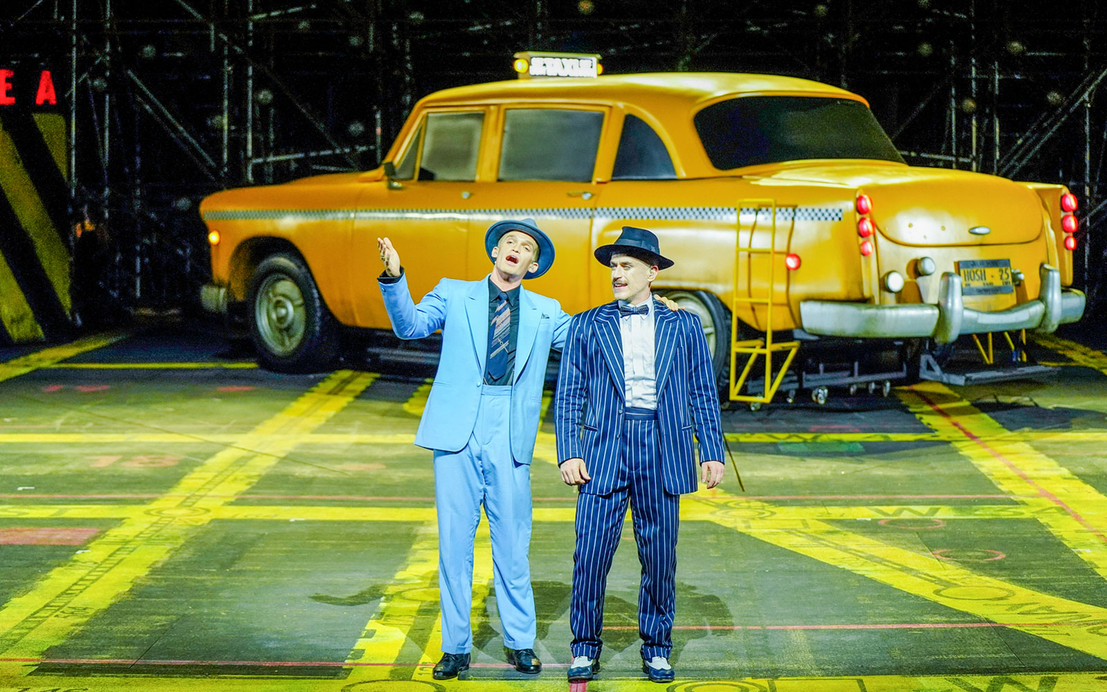 Performers in suits on stage with a yellow taxi backdrop, Guys & Dolls on Sydney Harbour.