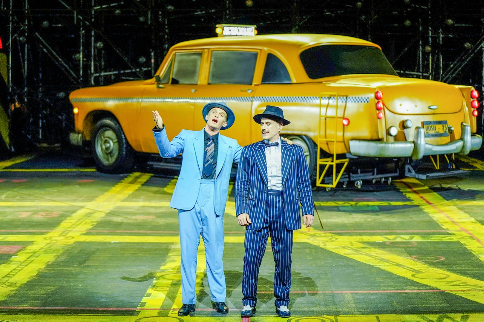 Performers in suits on stage with a yellow taxi backdrop, Guys & Dolls on Sydney Harbour.