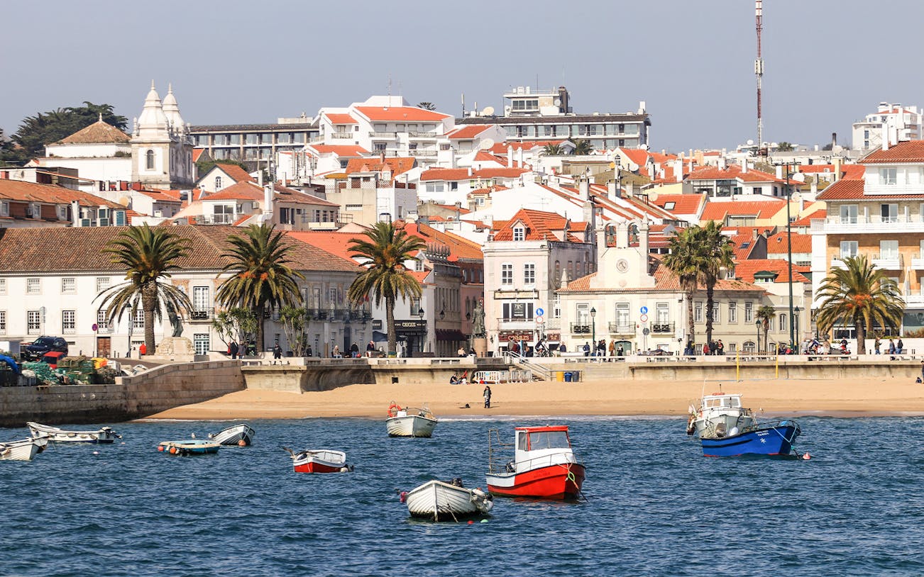 Boats in the harbor of Cascais fishing village, Portugal, with coastal buildings in the background.