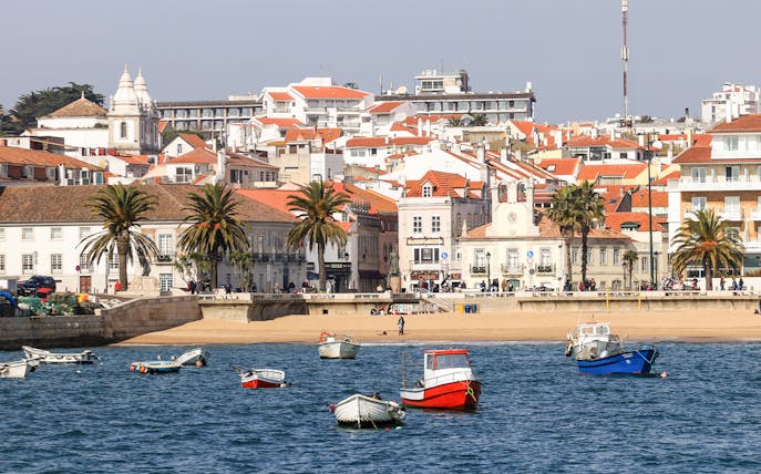 Boats in the harbor of Cascais fishing village, Portugal, with coastal buildings in the background.