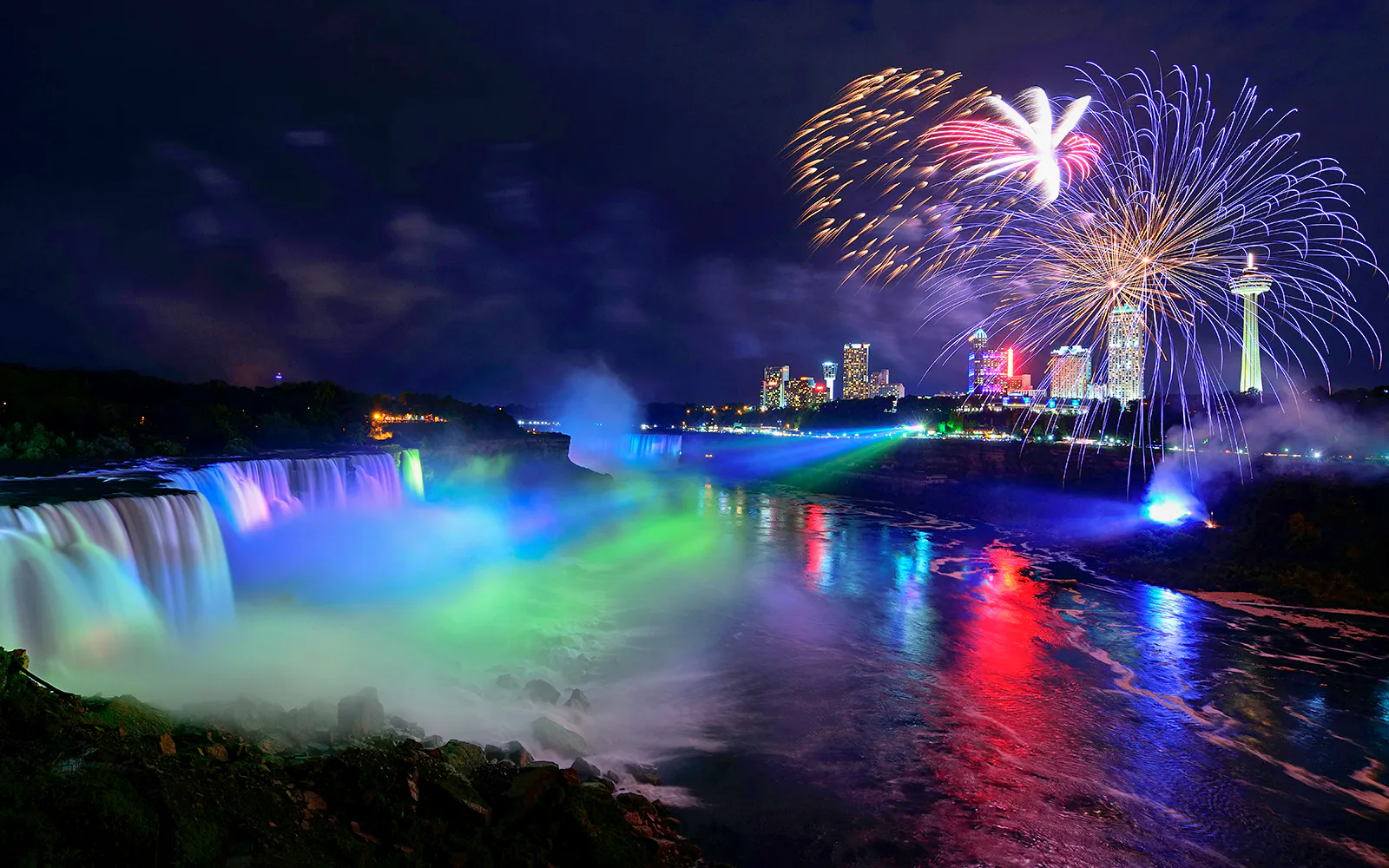 Niagara Falls illuminated at night with fireworks in the sky, USA evening tour.