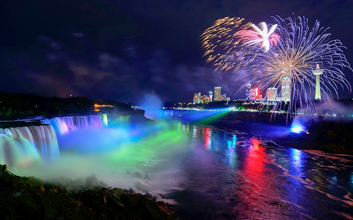 Niagara Falls illuminated at night with fireworks in the sky, USA evening tour.