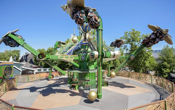 Aquila ride at Tivoli Gardens with passengers on rotating arms against a clear sky.
