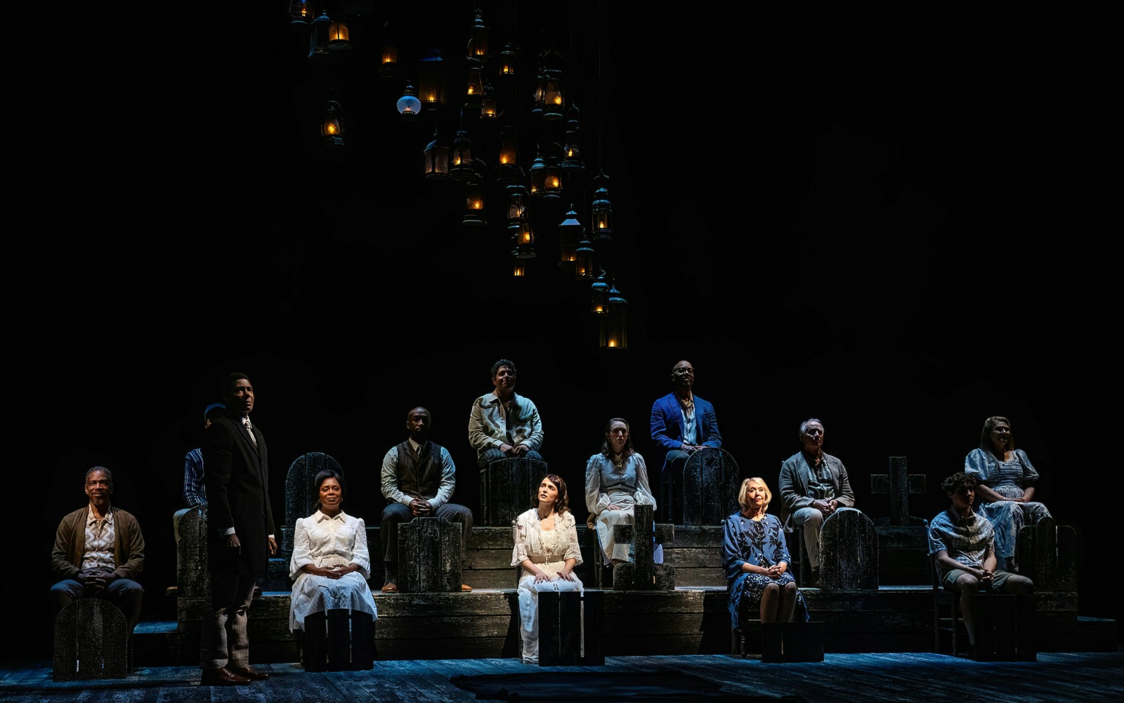 Cast of "Our Town" performing on stage with lanterns above.