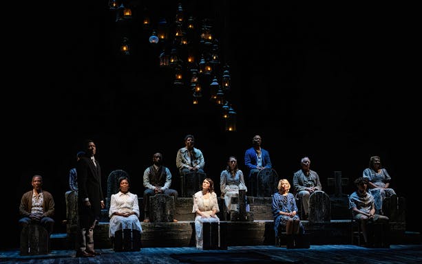 Cast of "Our Town" performing on stage with lanterns above.
