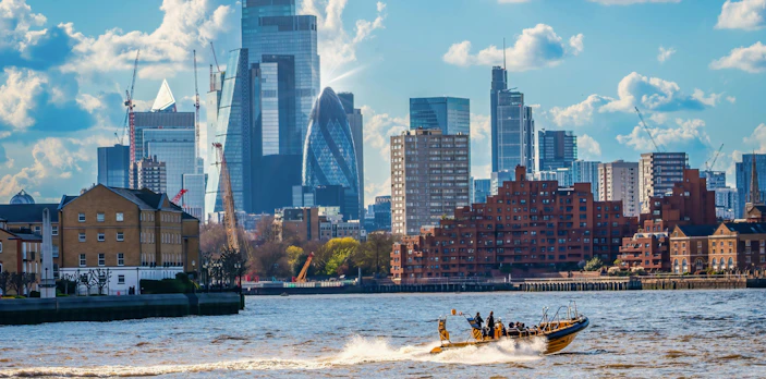 Speedboat on Thames River with London skyline in background.