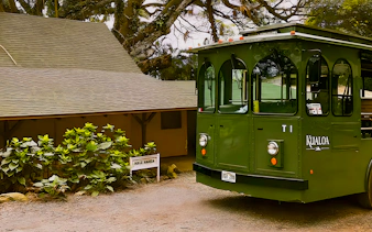 Kualoa Grown Tour trolley near Hale Nanea building surrounded by lush greenery.