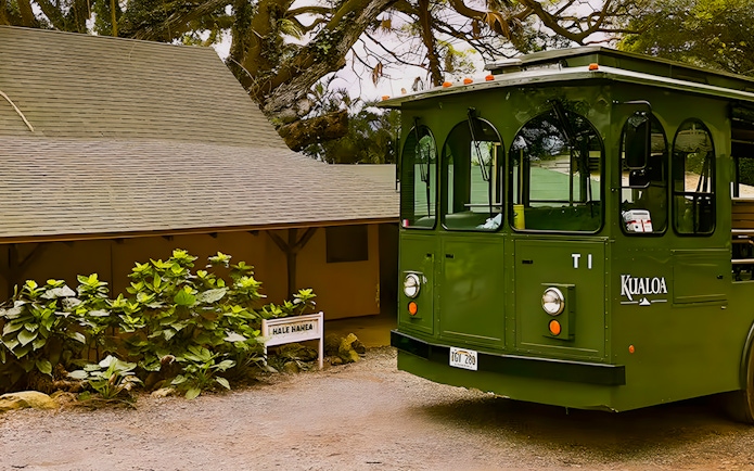 Kualoa Grown Tour trolley near Hale Nanea building surrounded by lush greenery.