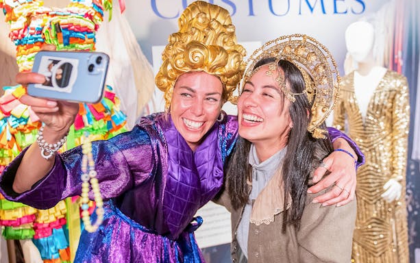 Visitors in colorful costumes taking a selfie at a museum exhibit during Globe Story and Guided Tours.
