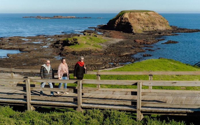 Visitors walking on a boardwalk at Phillip Island with ocean and rocky coastline views.