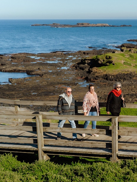 Visitors walking on a boardwalk at Phillip Island with ocean and rocky coastline views.