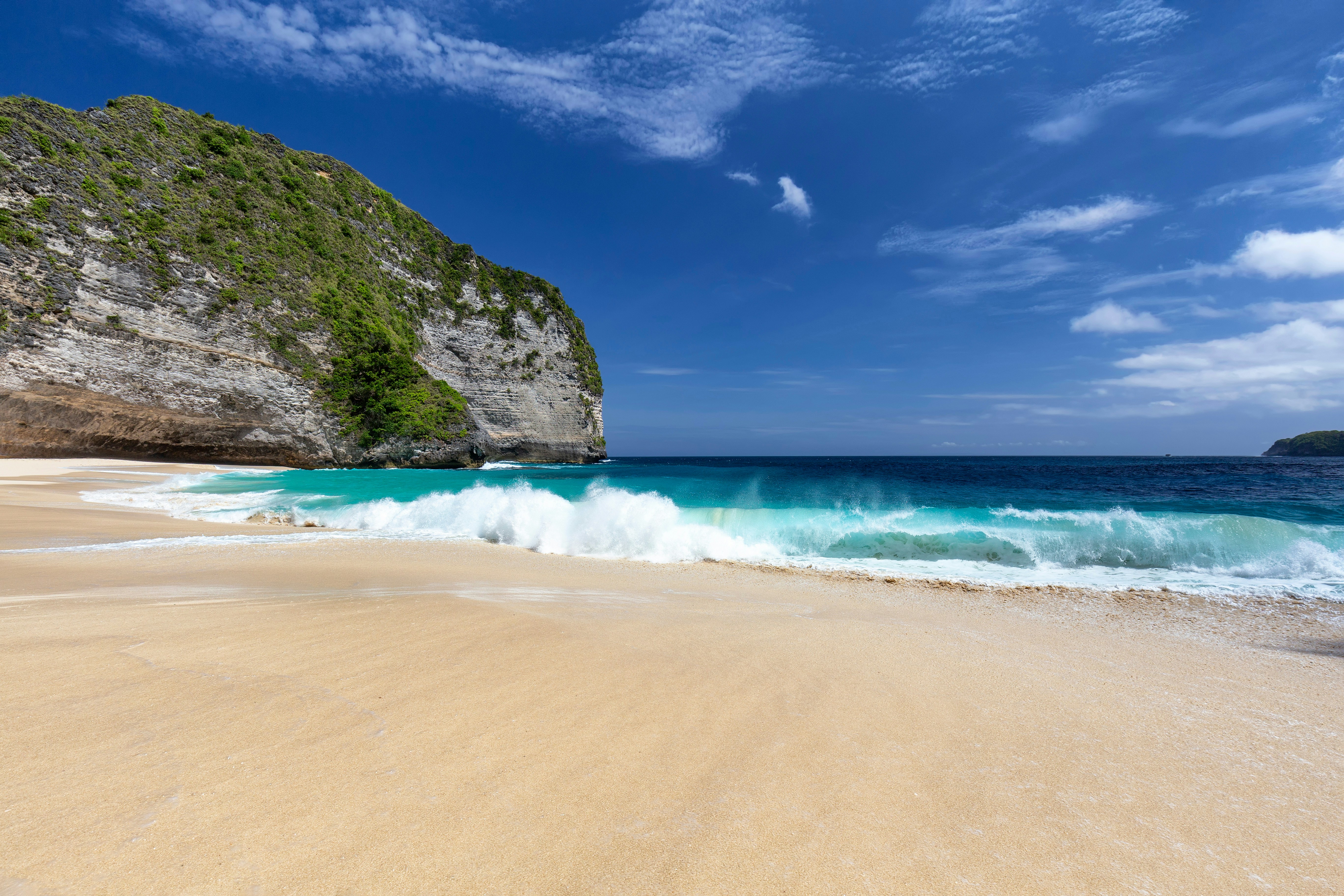 Waves crashing on the sandy shore of Kelingking Beach, Nusa Penida, Indonesia.