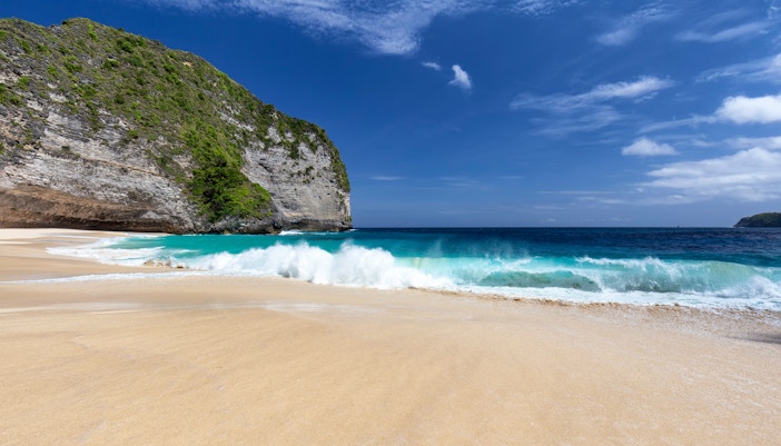Waves crashing on the sandy shore of Kelingking Beach, Nusa Penida, Indonesia.