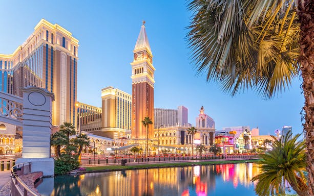 Las Vegas Strip with Venetian Resort and palm trees reflecting in water at dusk.