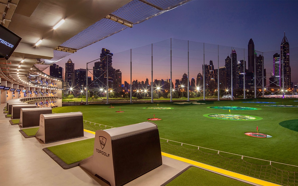 Topgolf Dubai driving range with city skyline at sunset.