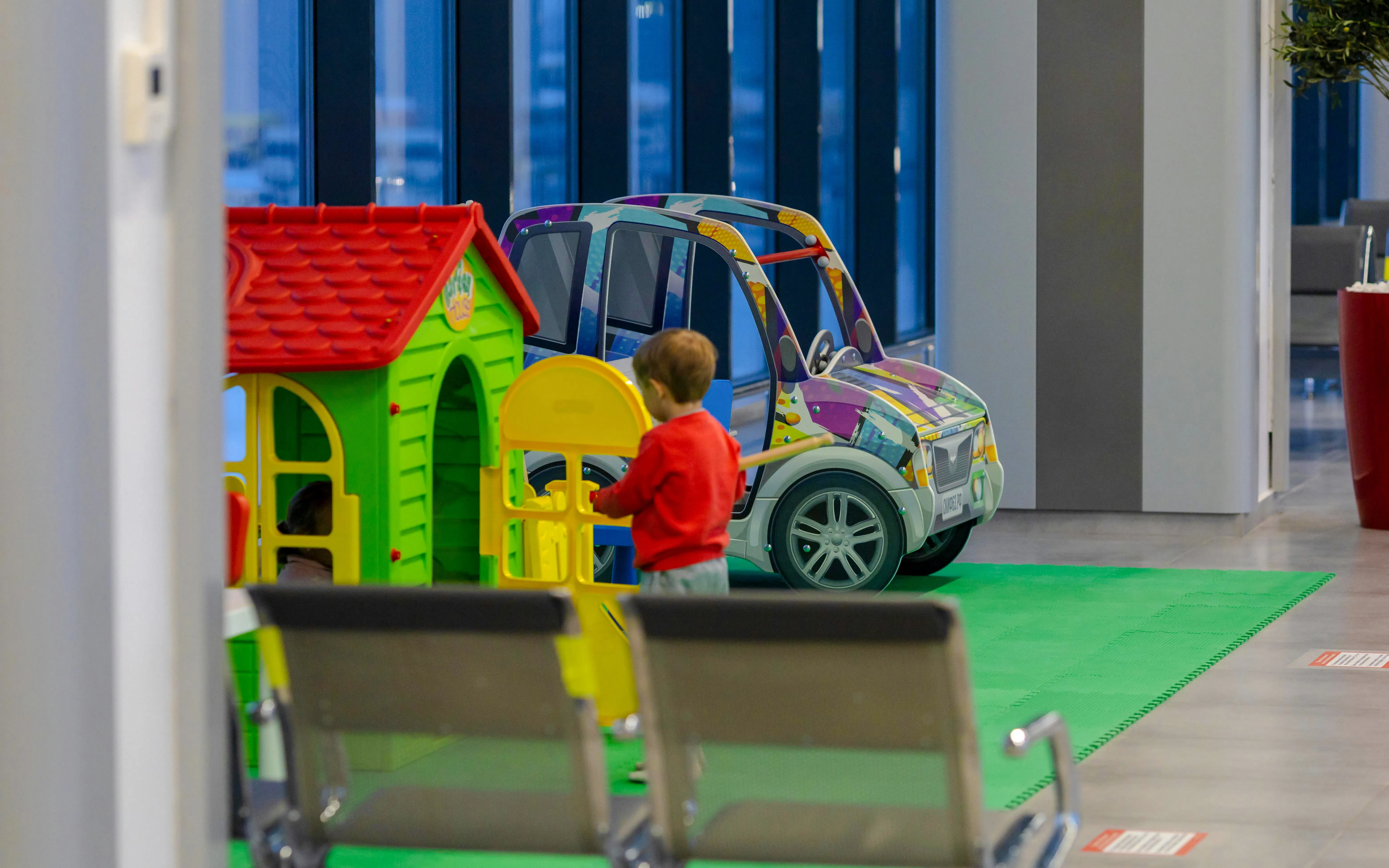 Child playing in airport lounge play area with toy house and car.