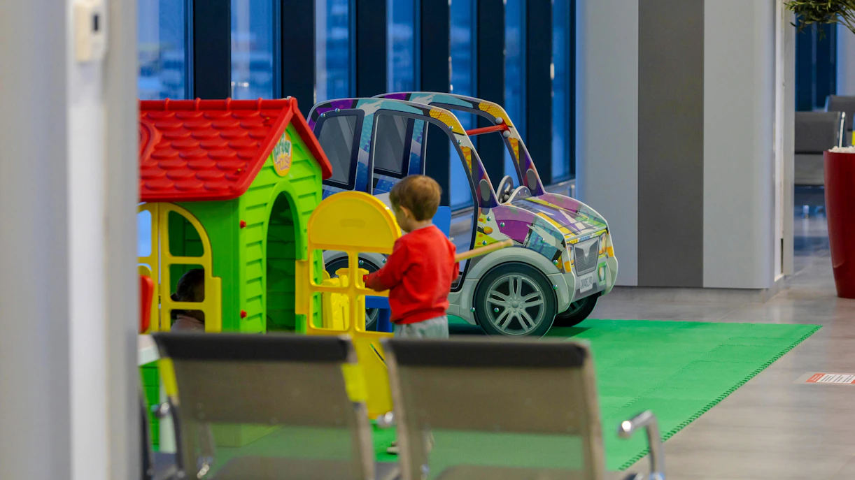 Child playing in airport lounge play area with toy house and car.