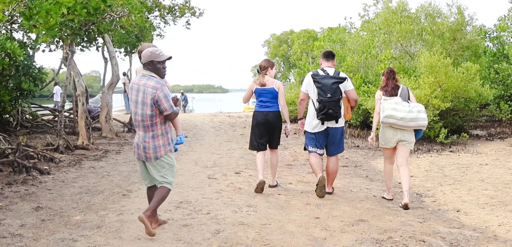 Tourists walking on a sandy path towards Funzi Island, surrounded by lush greenery, Diani Beach.