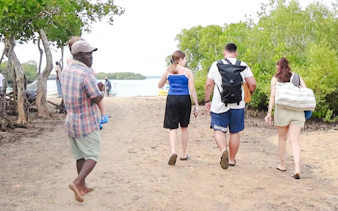 Tourists walking on a sandy path towards Funzi Island, surrounded by lush greenery, Diani Beach.