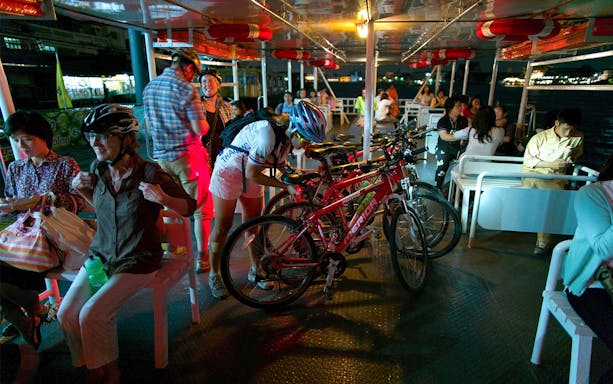 Cyclists with bikes on a ferry during Bangkok night bike tour.