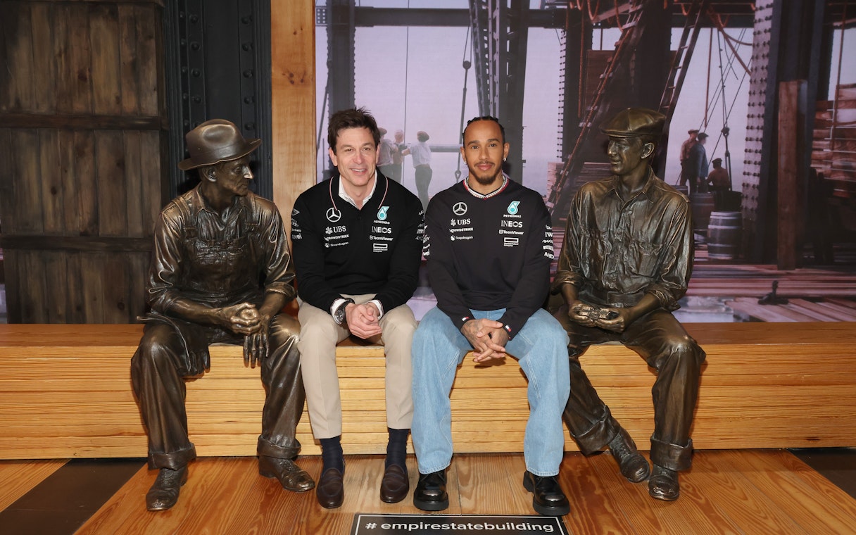 Two people seated between bronze worker statues at the Empire State Building.