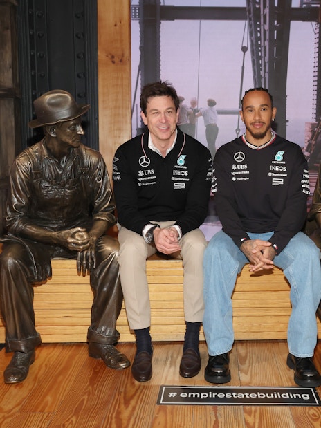 Two people seated between bronze worker statues at the Empire State Building.