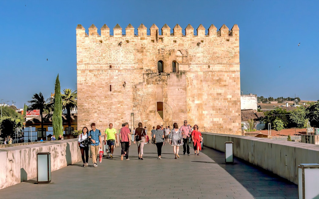 Visitors walking towards the historic gate of the Cordoba Mosque-Cathedral on a sunny day.