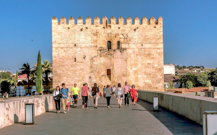 Visitors walking towards the historic gate of the Cordoba Mosque-Cathedral on a sunny day.