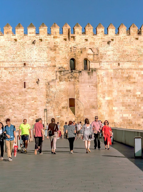 Visitors walking towards the historic gate of the Cordoba Mosque-Cathedral on a sunny day.