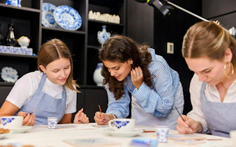 Guests painting tiles at a Dutch blue tile workshop, surrounded by traditional ceramics.