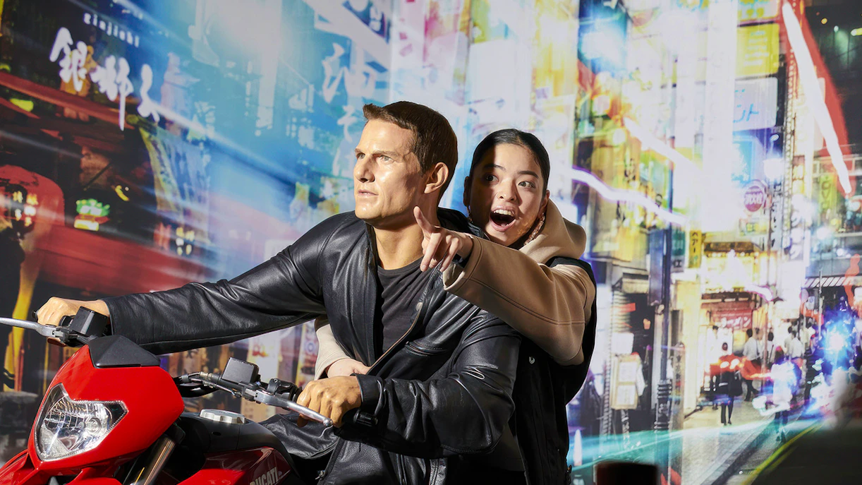 Wax figure on motorcycle at Madame Tussauds Tokyo with excited visitor.
