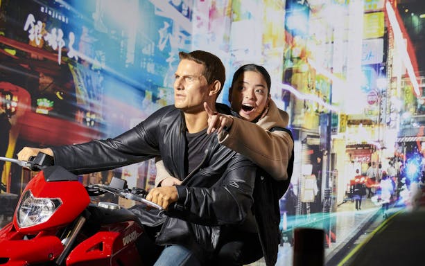 Wax figure on motorcycle at Madame Tussauds Tokyo with excited visitor.