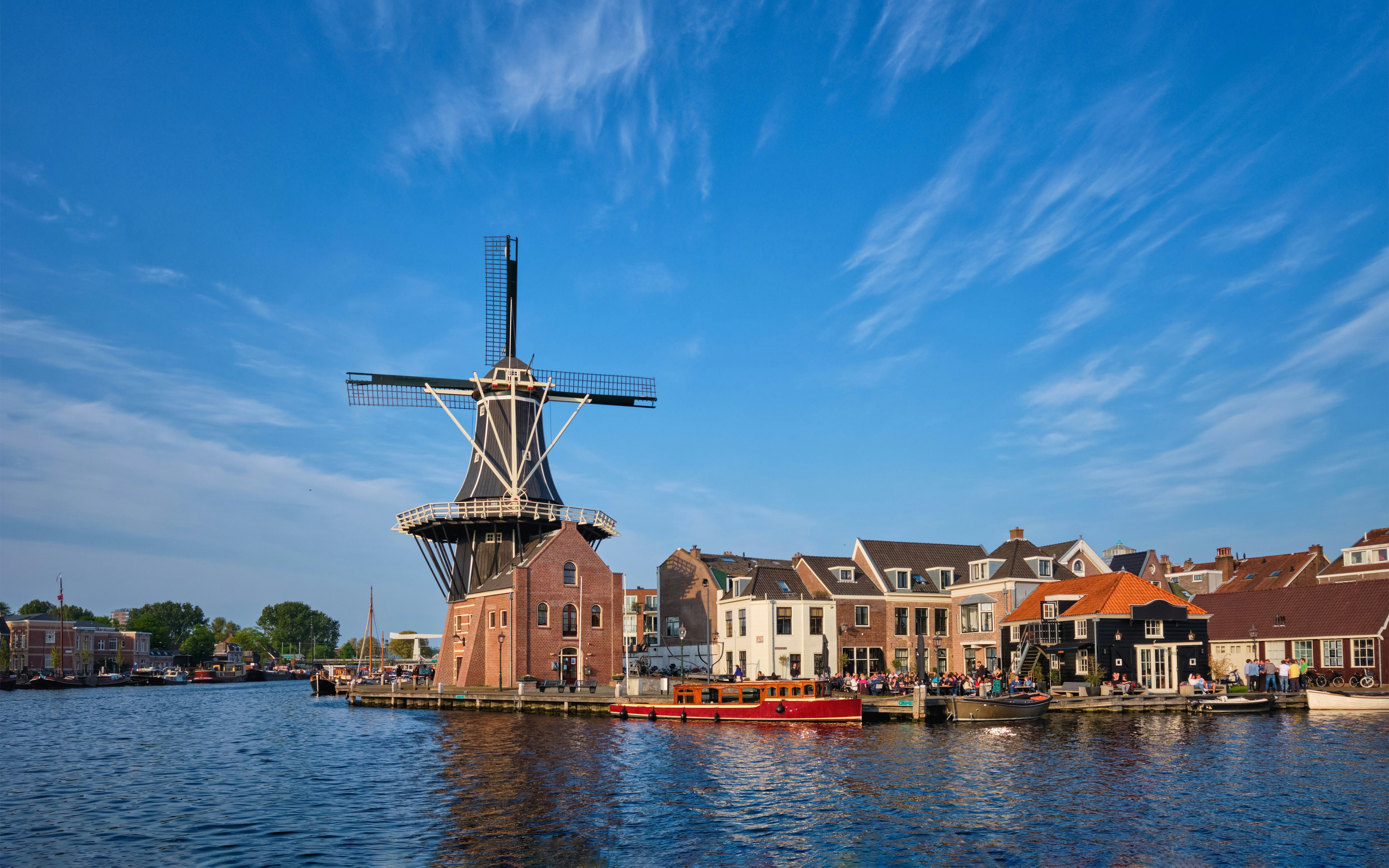 Windmill De Adriaan on Spaarne River with boats and nearby buildings in Haarlem, Netherlands.