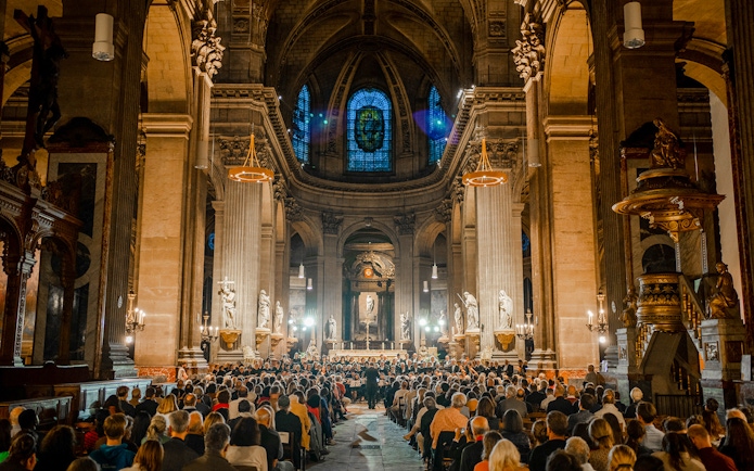 Orchestra performing in St Sulpice Church, Paris, with audience seated in the nave.