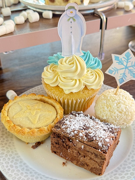 Cupcake with snowman topper, mince pie, brownie, and coconut treat on The Snowman Afternoon Tea Bus.