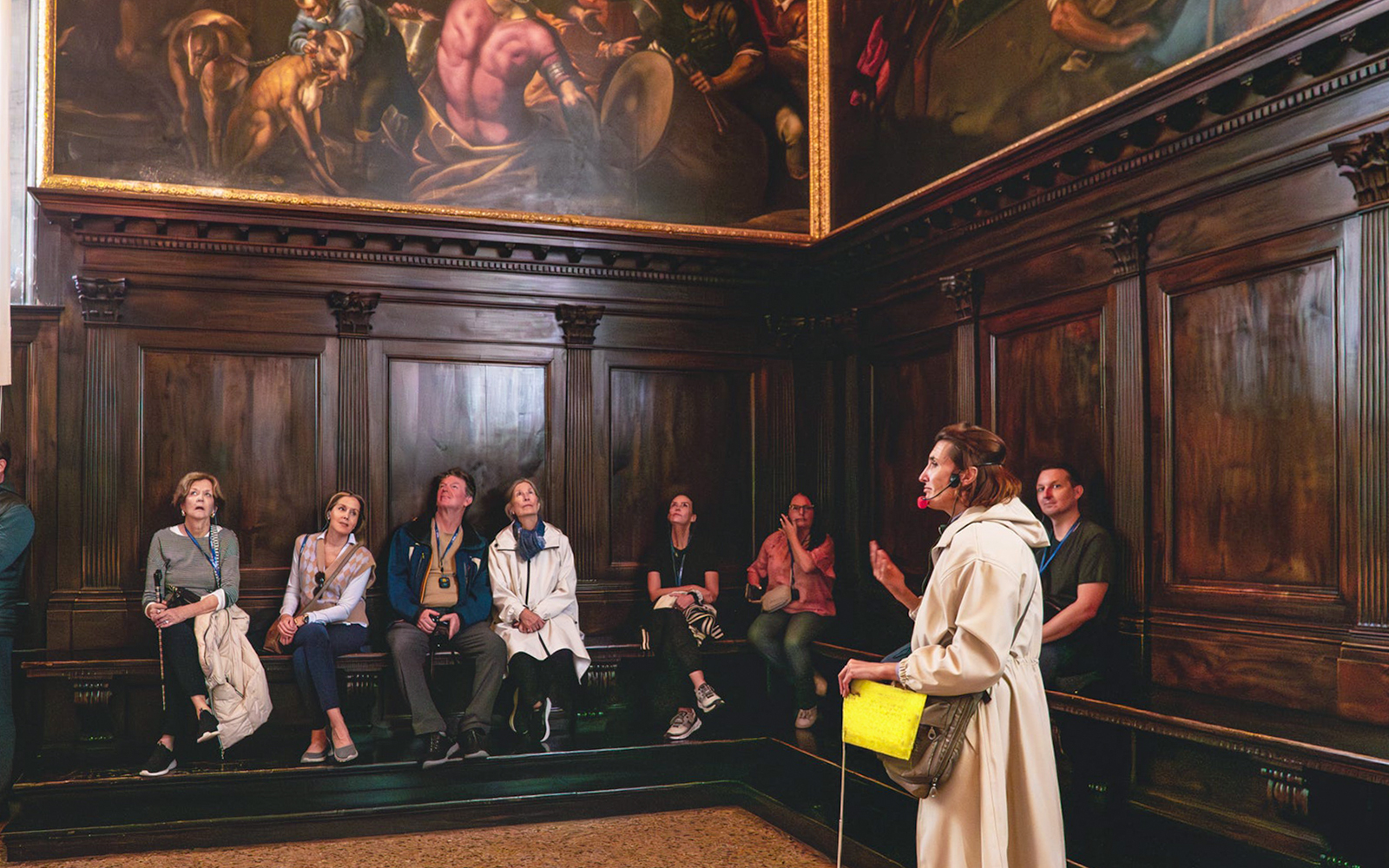Tour group listening to a guide in a room with ornate paintings at Doge's Palace, Venice.