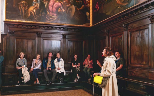 Tour group listening to a guide in a room with ornate paintings at Doge's Palace, Venice.