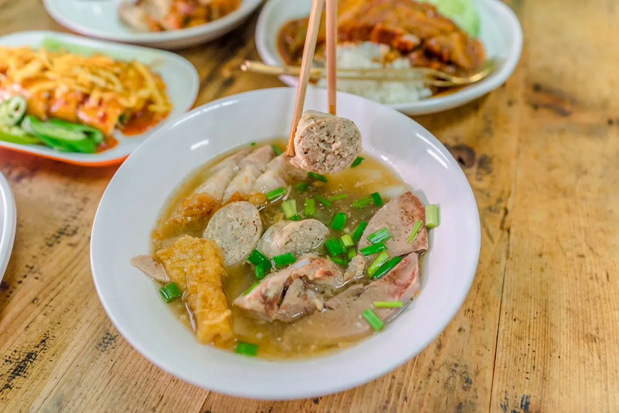 Chiang Mai street food dish with meat and vegetables in broth on a wooden table.