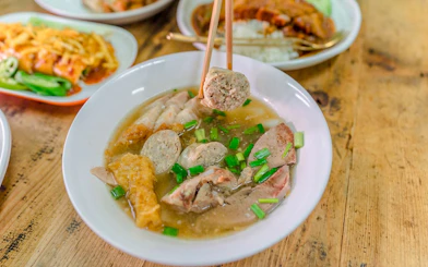 Chiang Mai street food dish with meat and vegetables in broth on a wooden table.