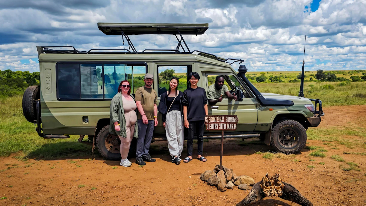 Safari group with guide and jeep at Masai Mara, Kenya, near Tanzania border sign.
