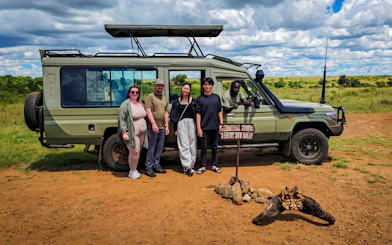 Safari group with guide and jeep at Masai Mara, Kenya, near Tanzania border sign.